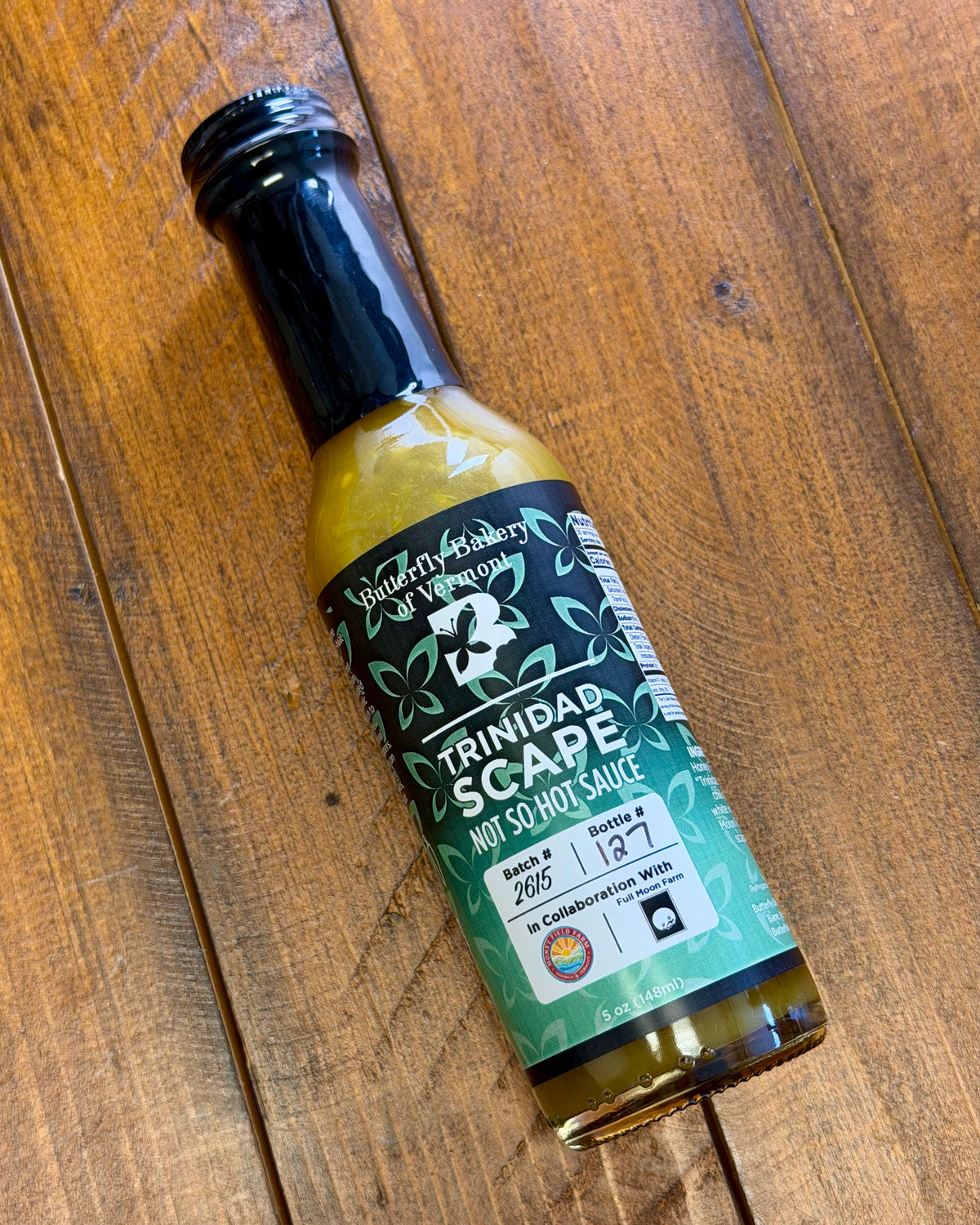 Bottle of Trinidad Garlic Scape sauce from Butterfly Bakery of Vermont on a wooden tabletop