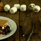 S'more made with Fat Toad Farm caramel on a white plate with marshmallows and graham crackers in the background