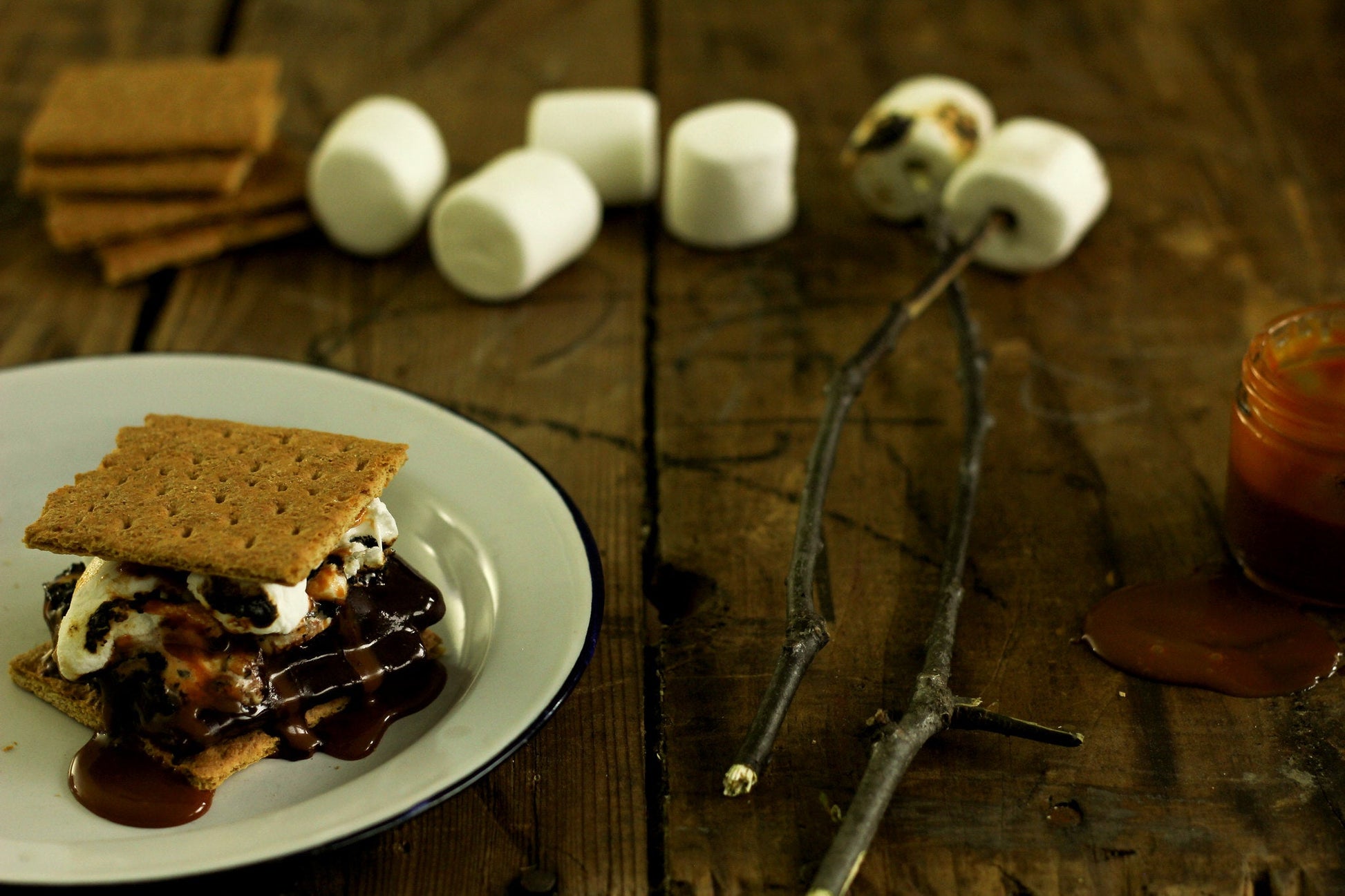 S'more made with Fat Toad Farm caramel on a white plate with marshmallows and graham crackers in the background