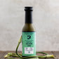 Bottle of Butterfly Bakery of Vermont Scape Sauce surrounded by garlic scapes on a wood table